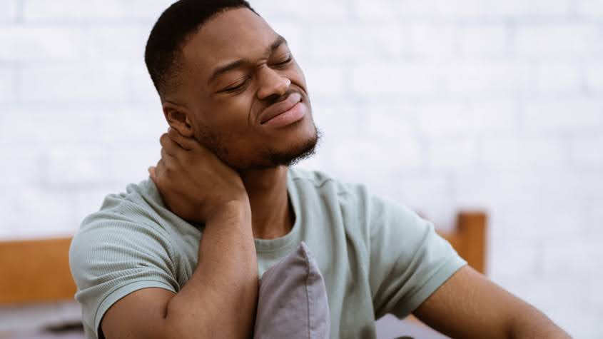 Individual with neck stiffness holding the back of his neck