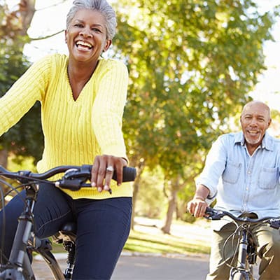 Happy elder couple on bikes riding through a park.