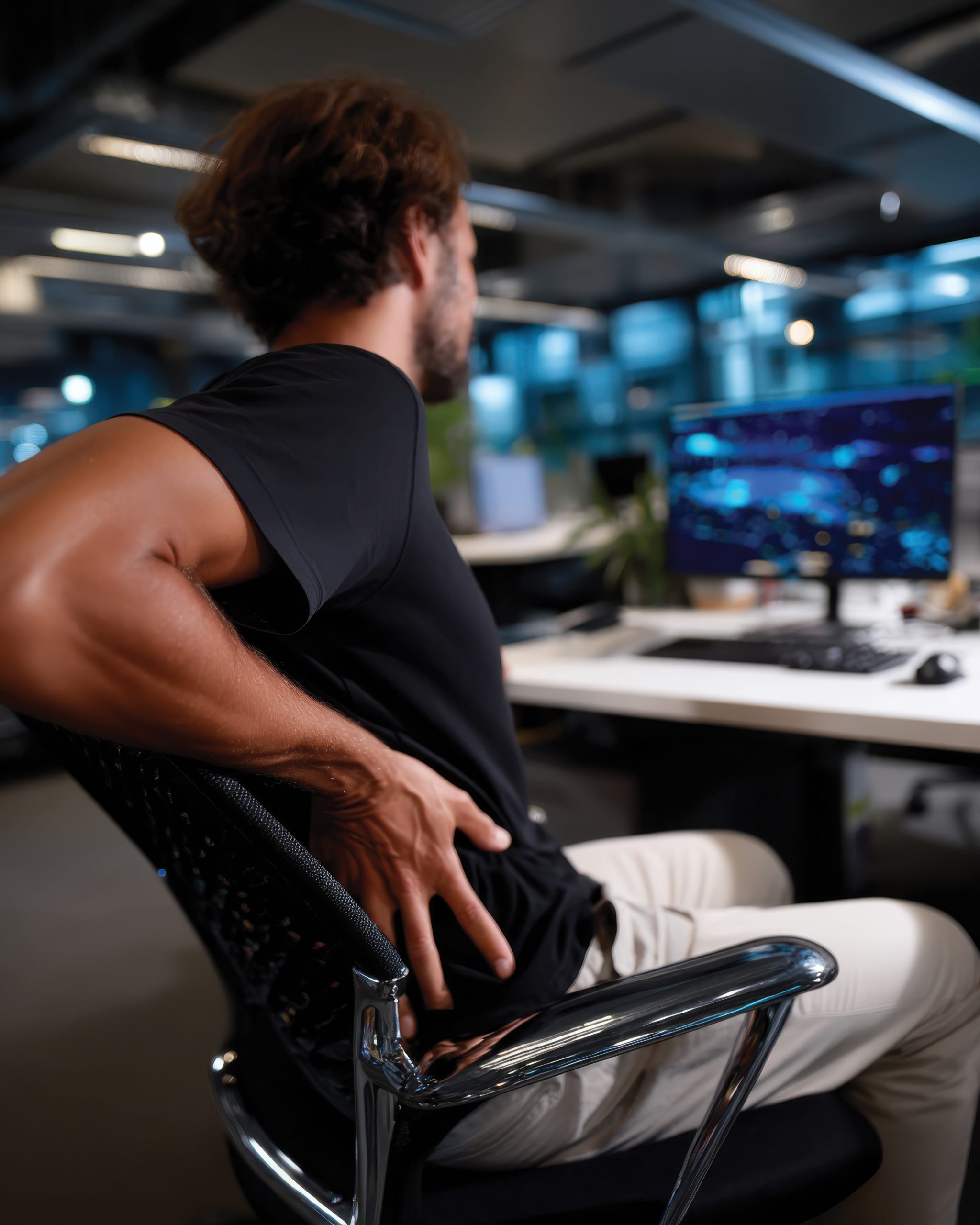 man sitting in chair at desk holding his side, showing pain
